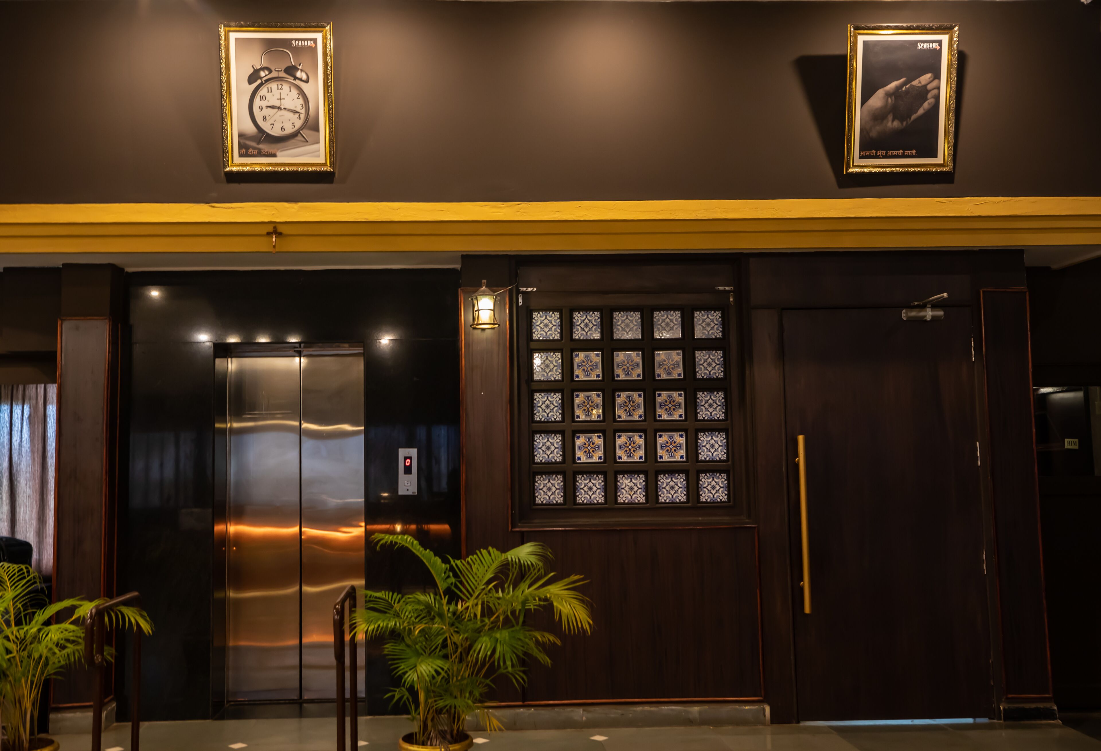 A hotel lobby with a modern elevator, a decorative wall with a clock, and a patterned door.