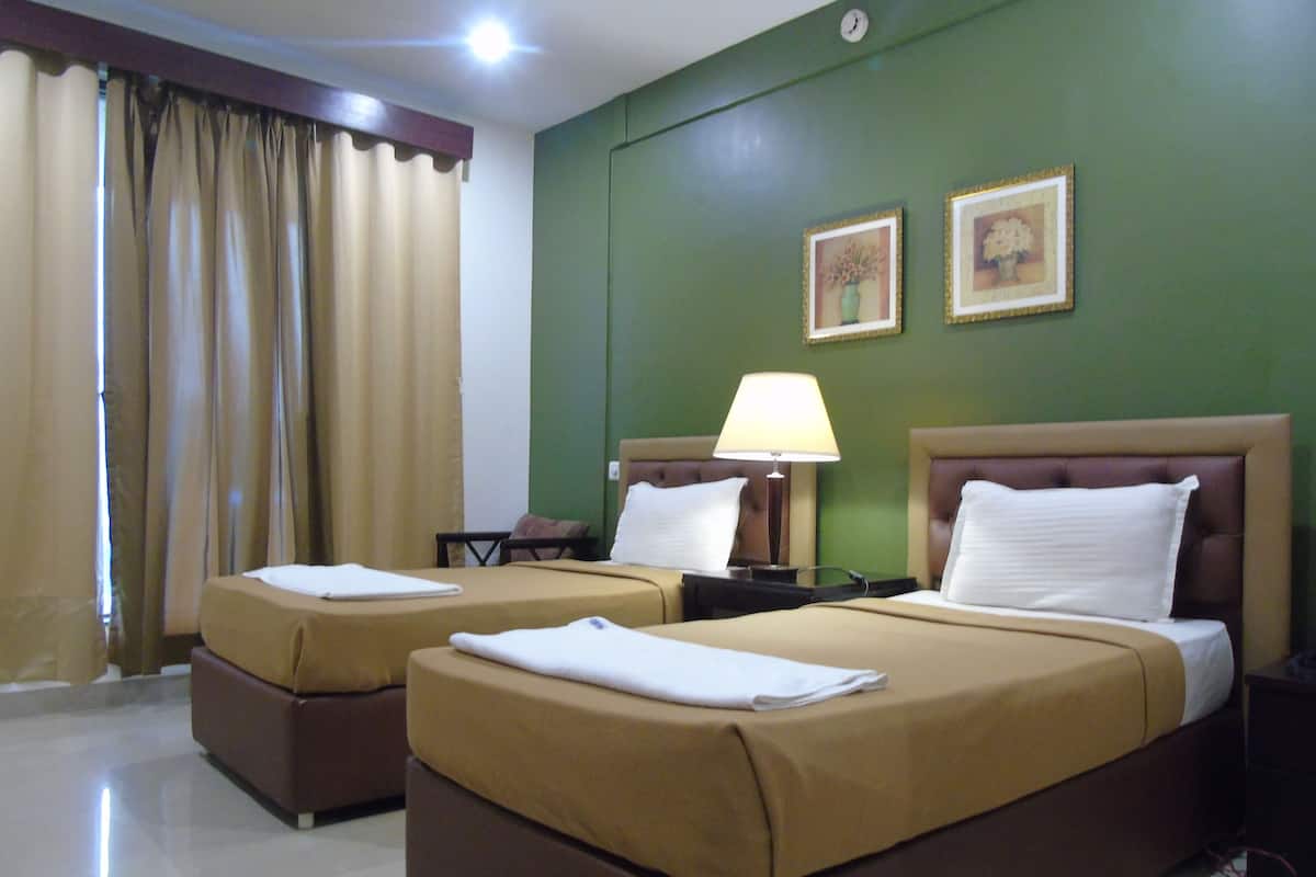 A hotel room with two beds, a nightstand with a lamp, a clock on the wall, and two framed pictures.