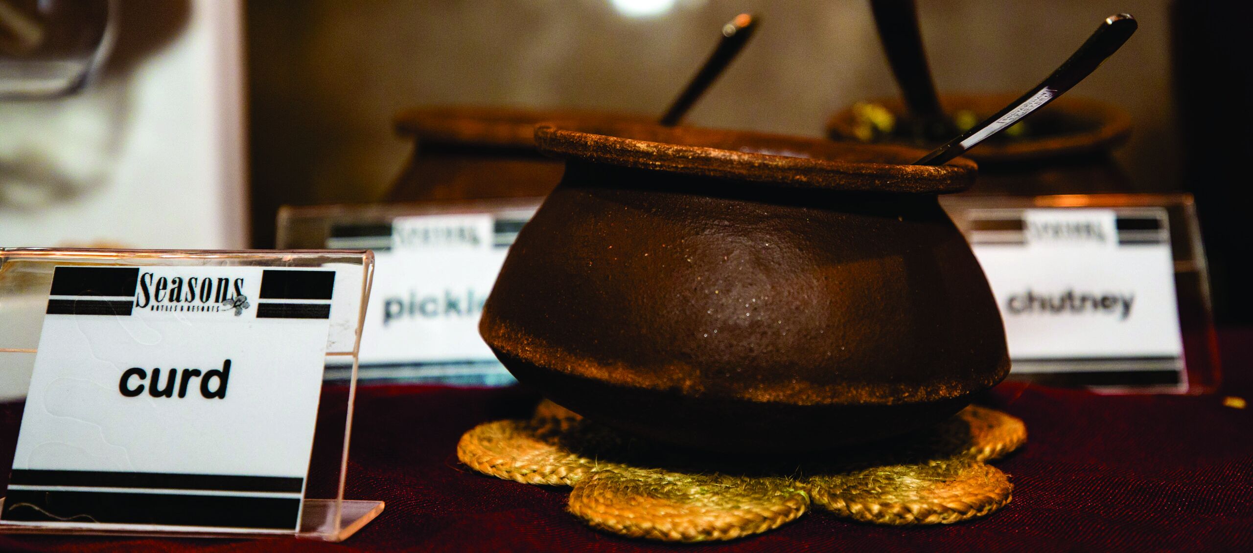A traditional copper pot on a woven mat with a label reading "curd".