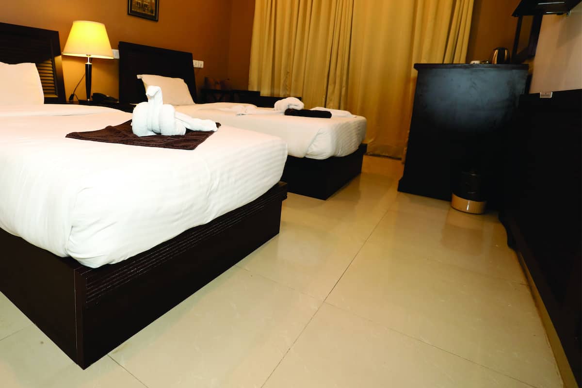 A hotel room with two beds, a nightstand, a lamp, and a minibar.