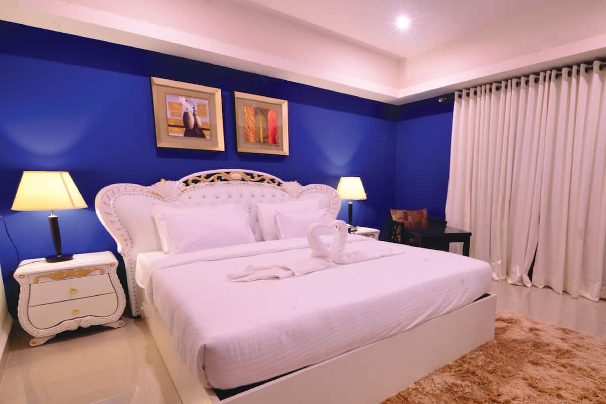 A bedroom with a white bed, two bedside lamps, a nightstand, a dresser, and a large window with white curtains.