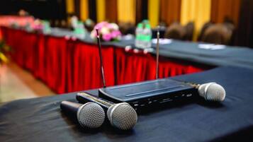 A conference table with microphones and a laptop, set against a red backdrop.