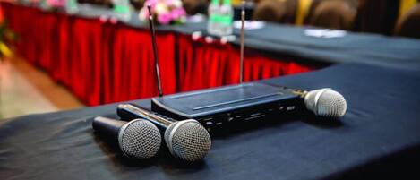 A conference table with microphones and a laptop, set against a red backdrop.