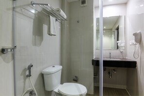 Un baño moderno con cabina de ducha de vidrio, inodoro blanco, lavabo con encimera negra y secador de pelo montado en la pared.
