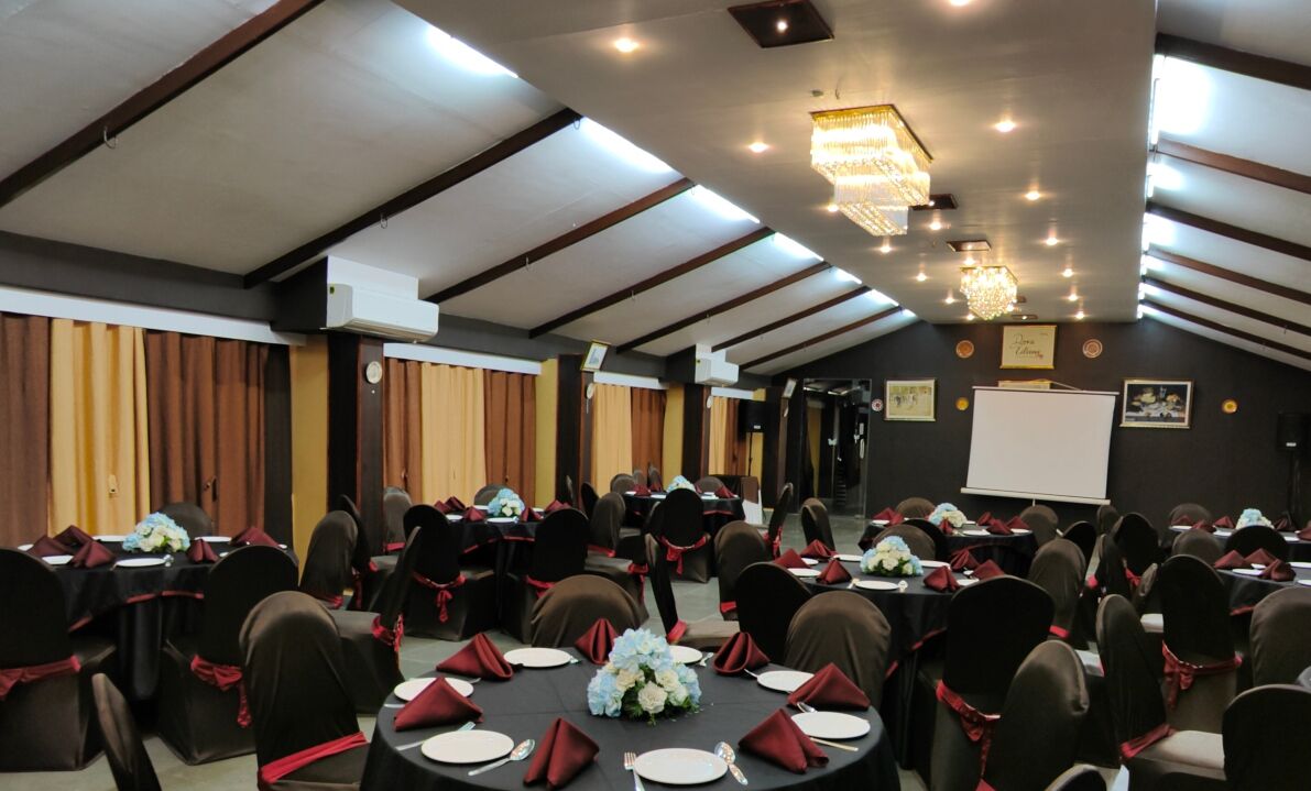 A conference room with round tables, black chairs with red sashes, and a chandelier.