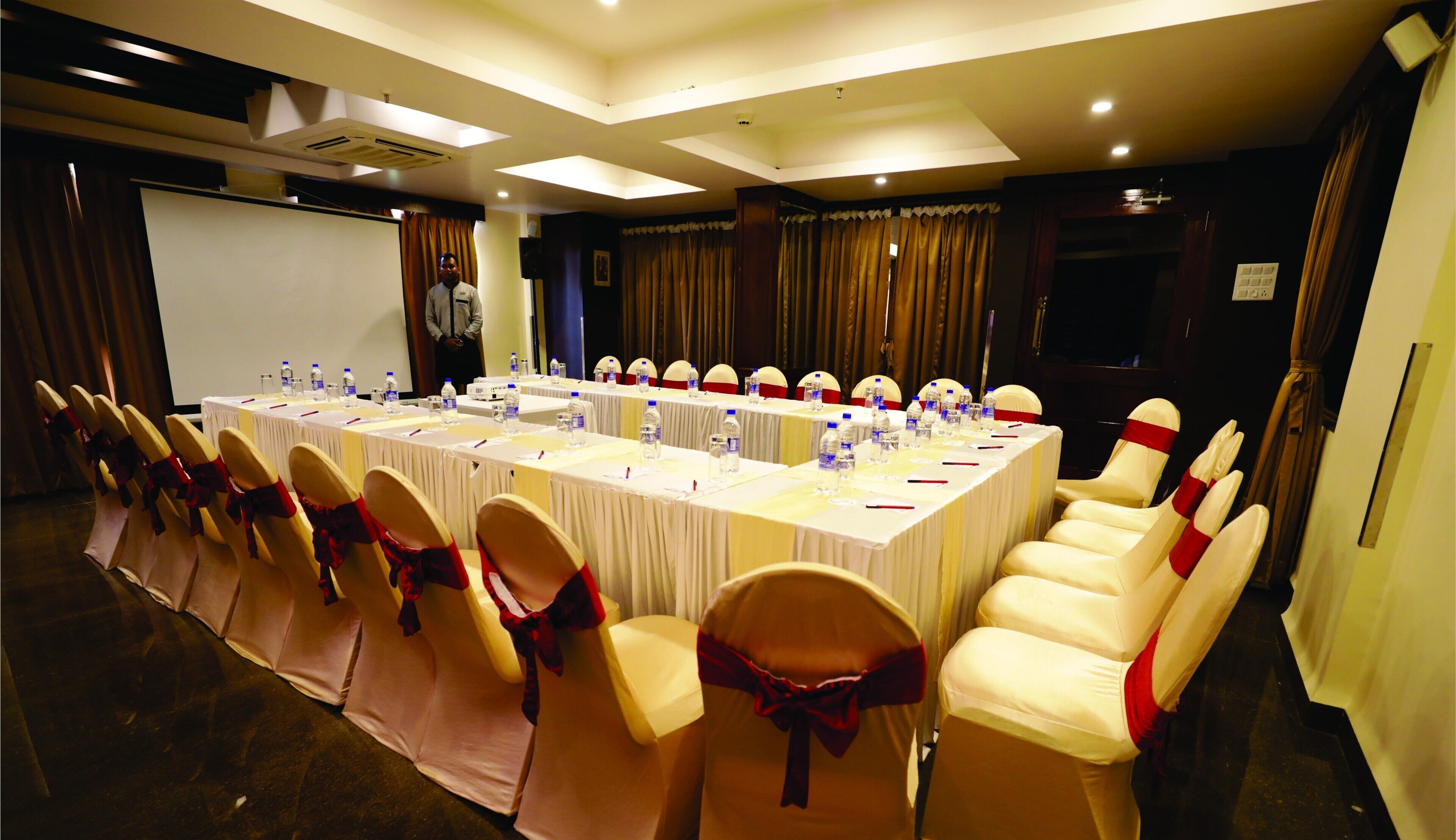 A conference room with a long table, chairs with red sashes, and water bottles.