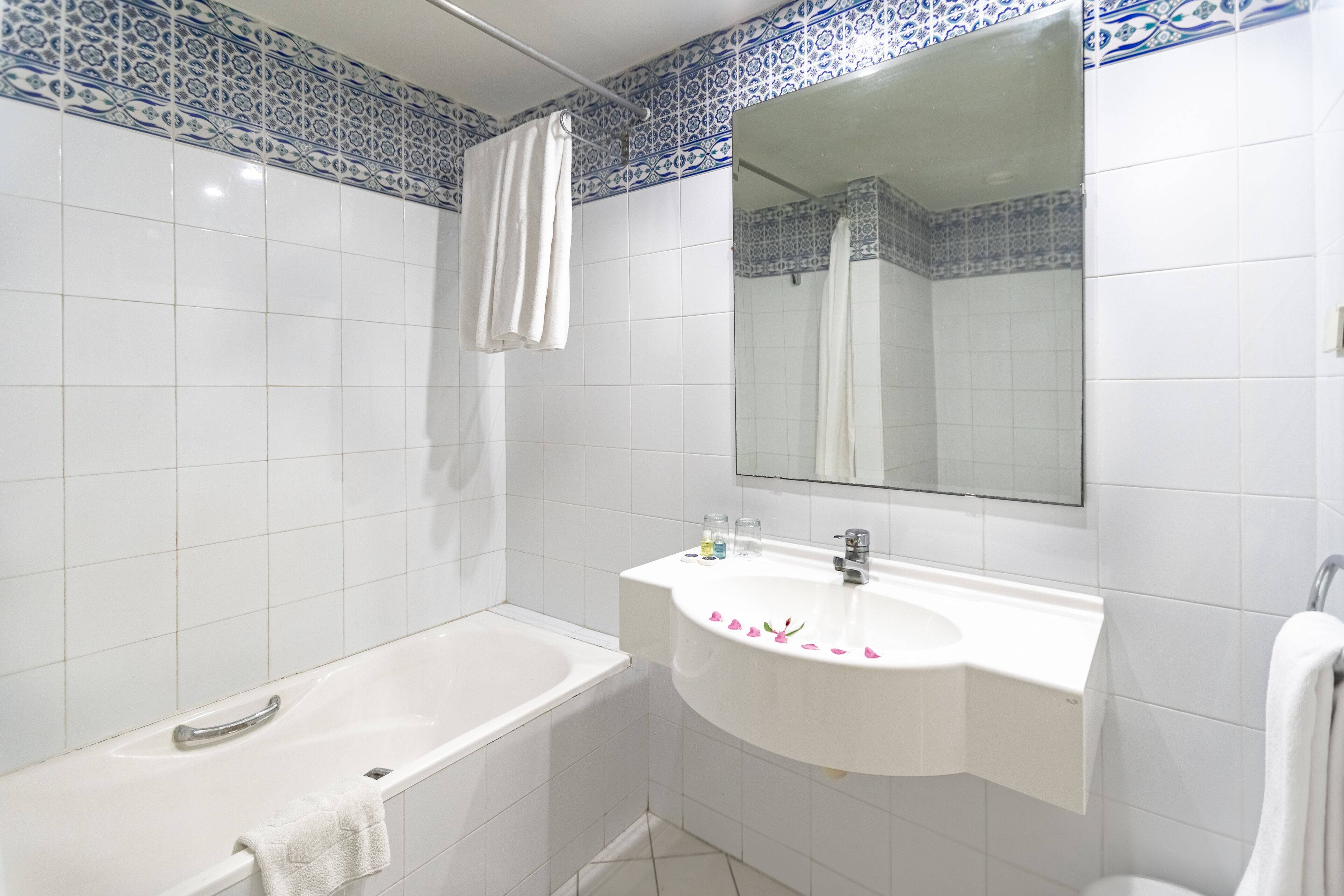 A bathroom with a white bathtub, a white sink with a mirror above it, and blue and white patterned tiles on the walls.