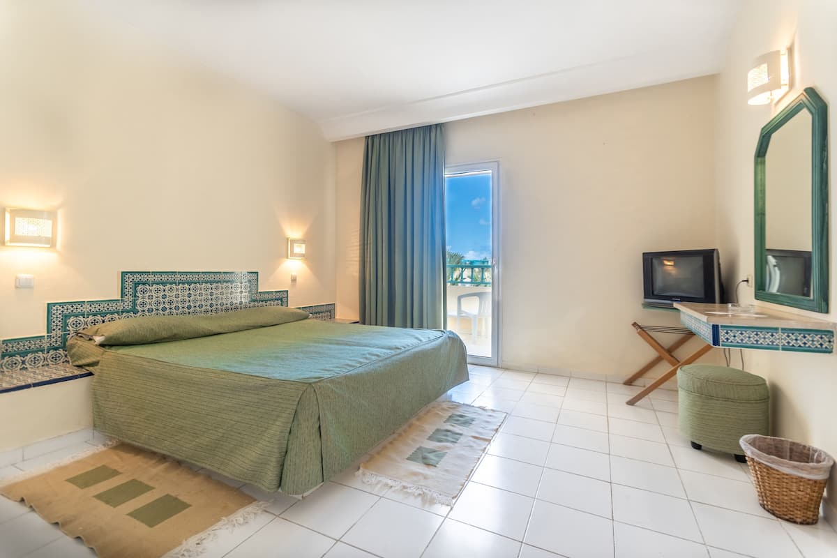 A bedroom with a bed, a television, a small table, a chair, and a balcony with a view.
