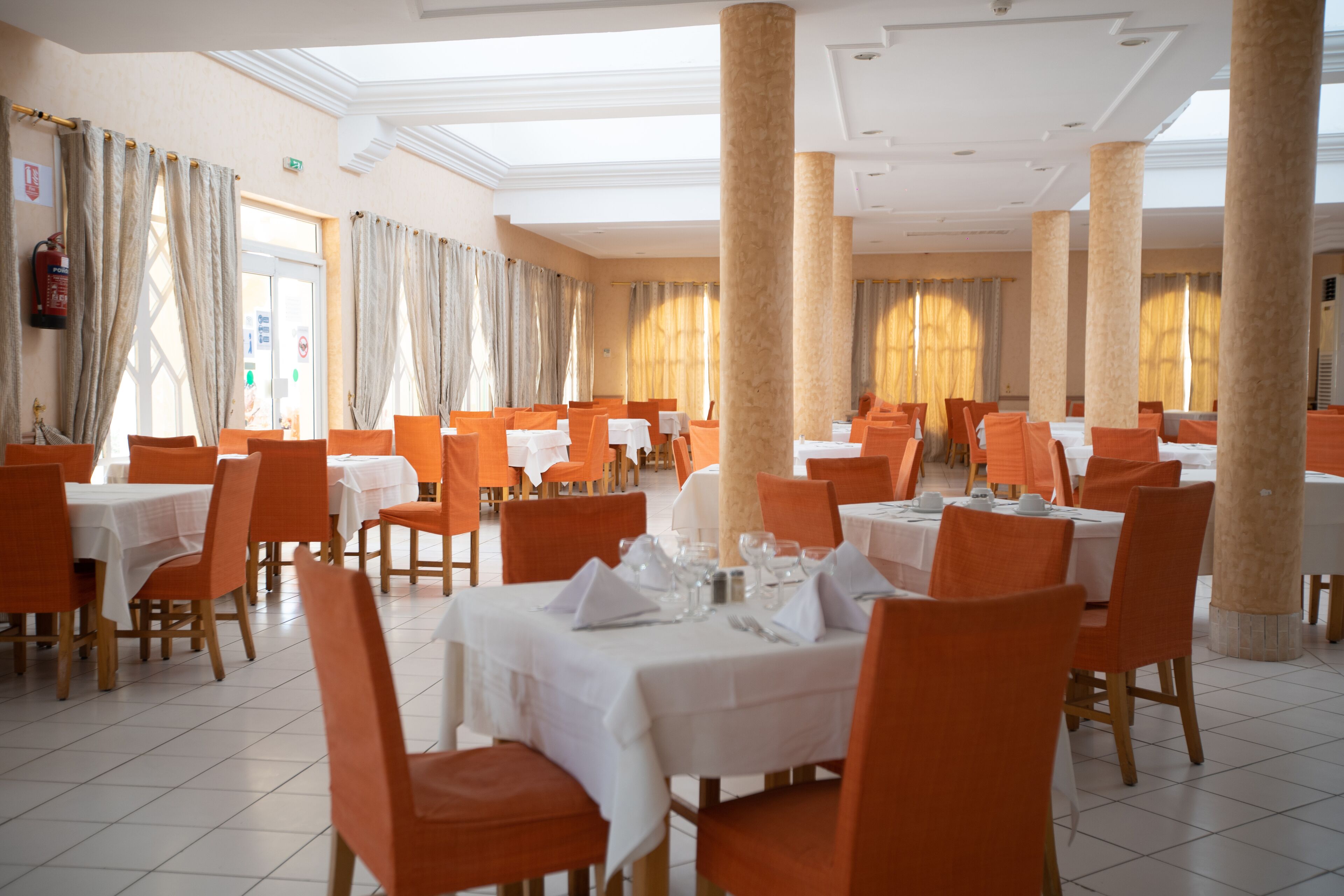 A dining area with multiple tables and chairs, large columns, and a high ceiling with skylights.