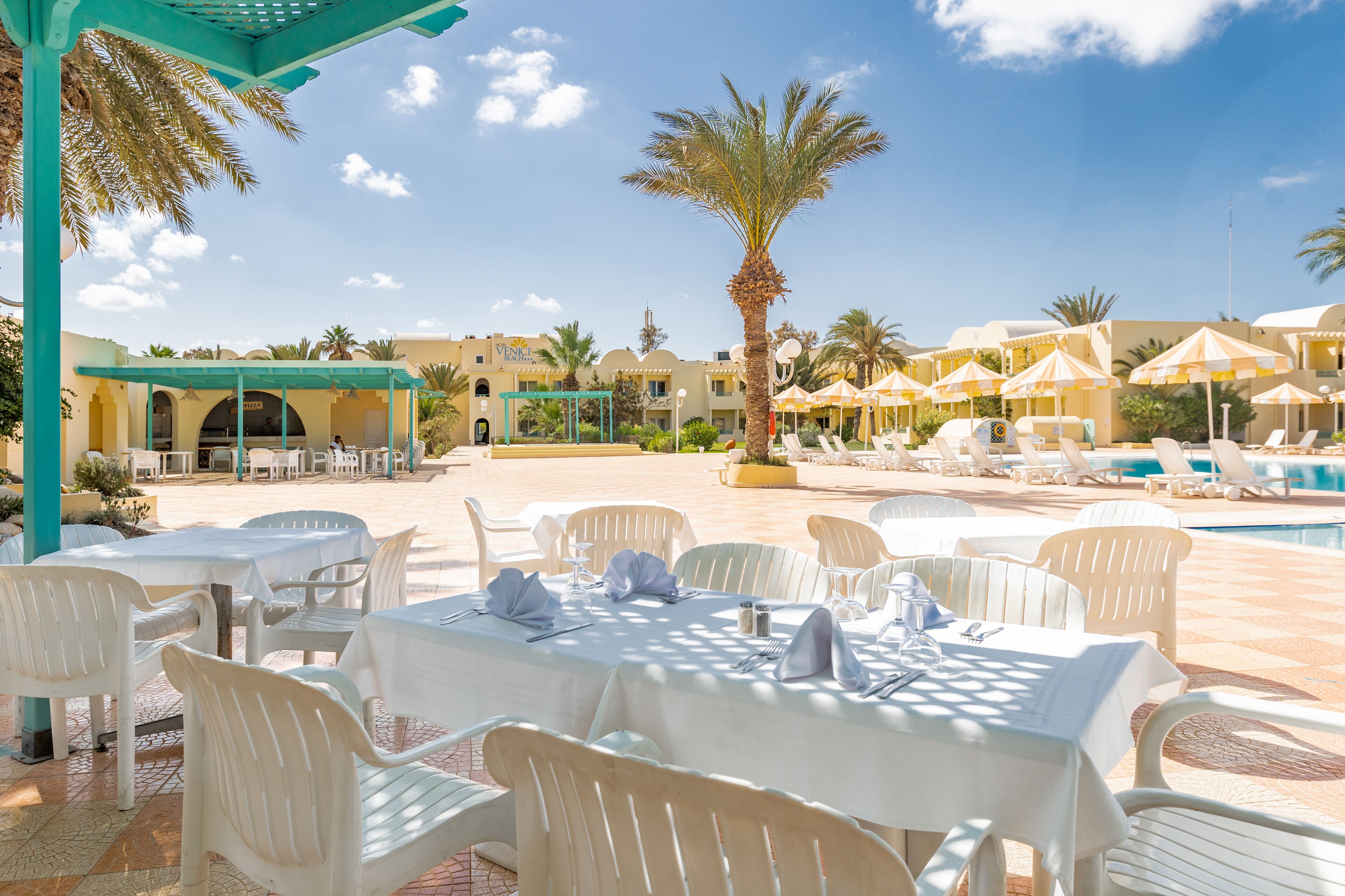 A resort with outdoor dining areas, a pool, and palm trees.
