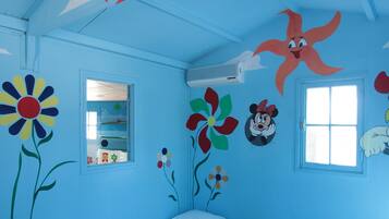 A child's bedroom with two single beds, a window, and wall decorations including flowers and cartoon characters.