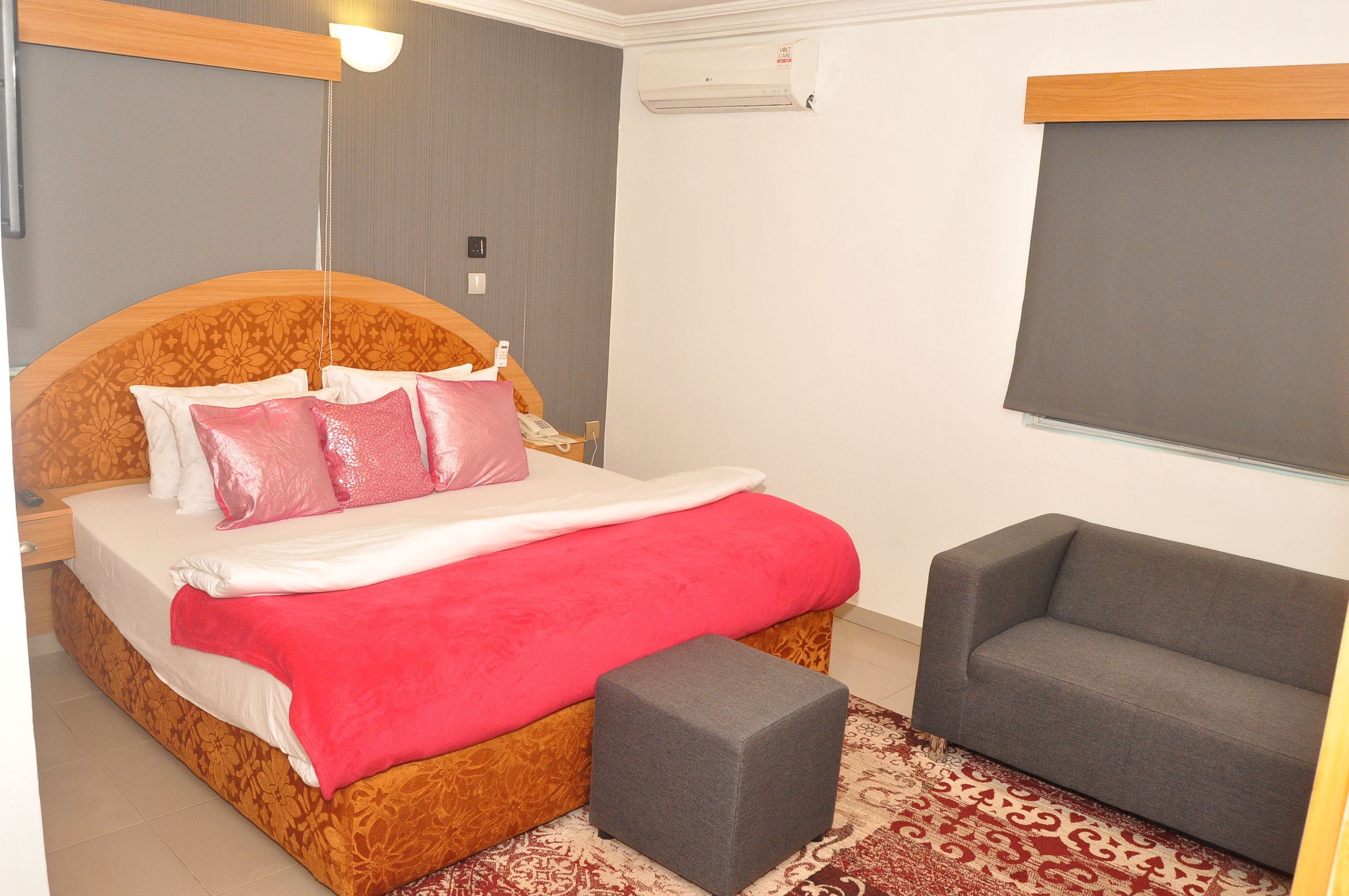 A bedroom with a bed, a grey sofa, and a patterned rug.