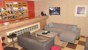 Una sala de estar con barra, un sofá gris, una mesita de centro y un reposapiés rojo.