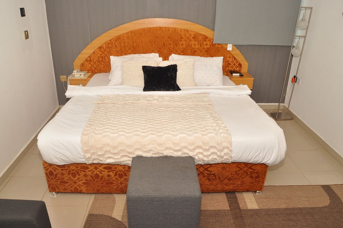 Una cama bien hecha con un cabecero estampado, una mesita de noche con una lámpara y un banco al pie de la cama.