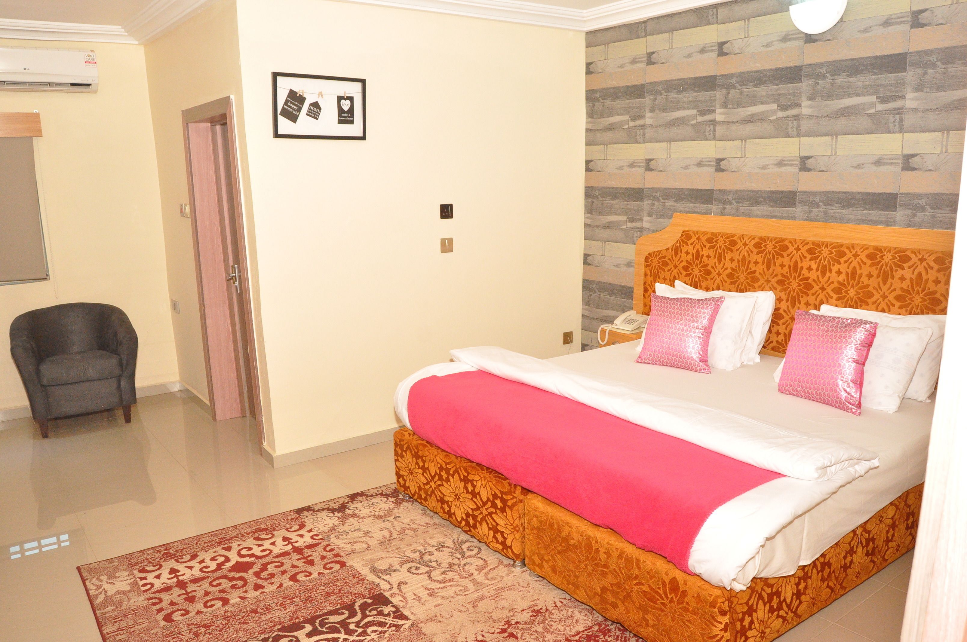 A hotel room with a large bed, a chair, a door, and a wall with a patterned design.