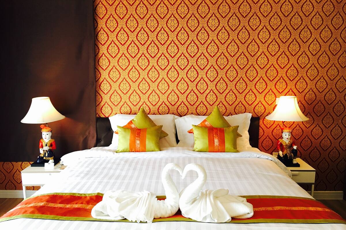 A hotel room with a large bed, two nightstands, decorative pillows, and a swan-shaped towel arrangement on the bed.