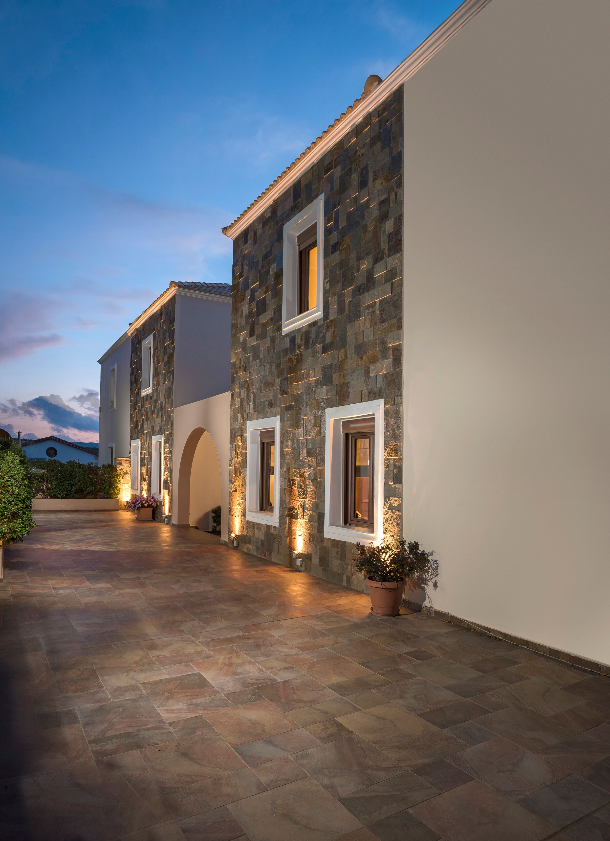 A stone building with arched doorways and illuminated windows, set against a twilight sky.