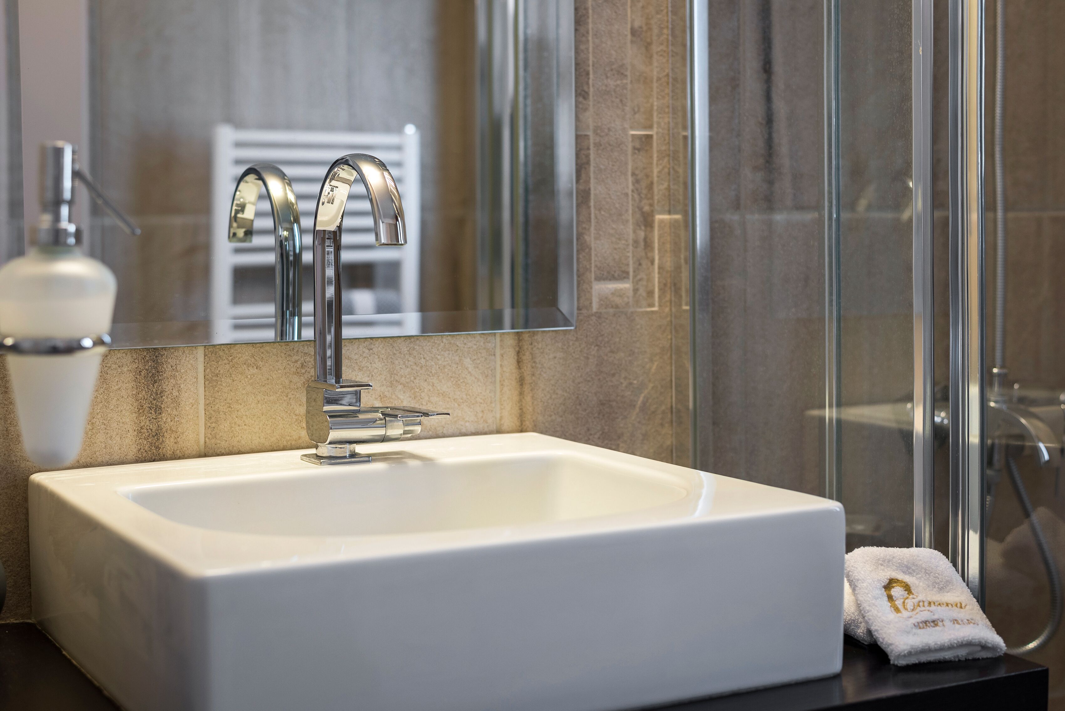 A modern bathroom with a white sink, chrome faucet, and a glass shower enclosure.