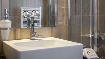 A modern bathroom with a white sink, chrome faucet, and a glass shower enclosure.
