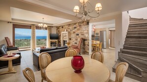 A spacious living area with a large round table, comfortable seating, a chandelier, and a view of the ocean. - Caneva Luxury Villa (Platanias)