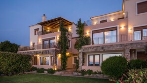 A two-story house with a balcony, stone facade, and well-lit windows. - Caneva Luxury Villa (Platanias)
