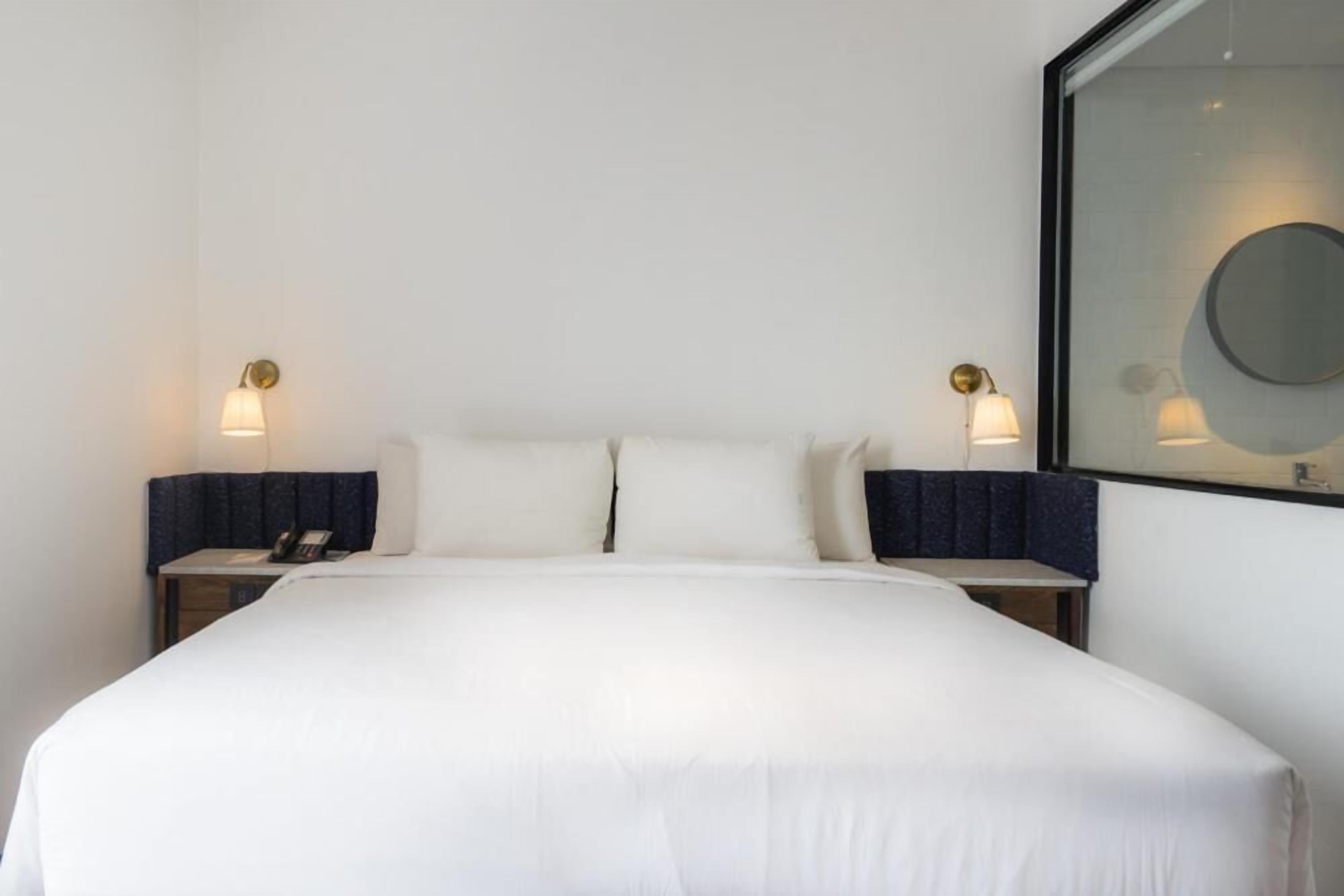 A neatly made bed with white linens, two bedside tables with lamps, and a large mirror on the wall.