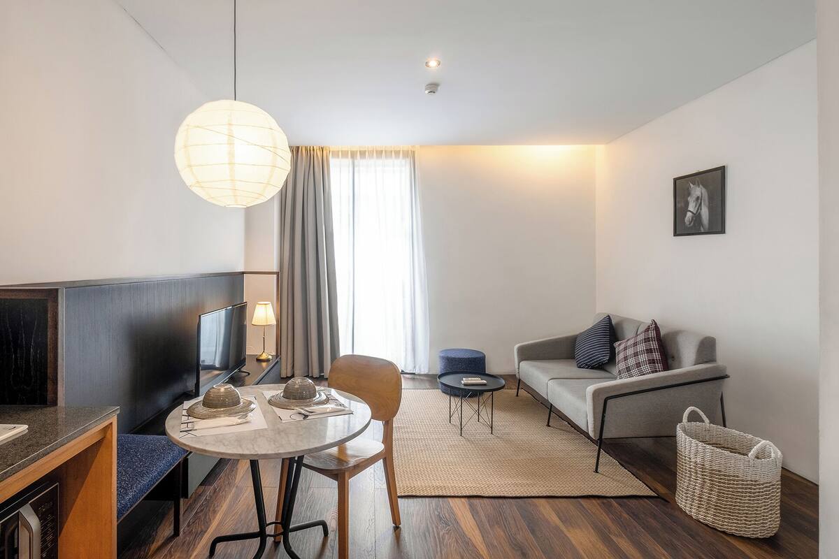 A modern hotel room with a dining area, a sofa, a lamp, and a picture on the wall.