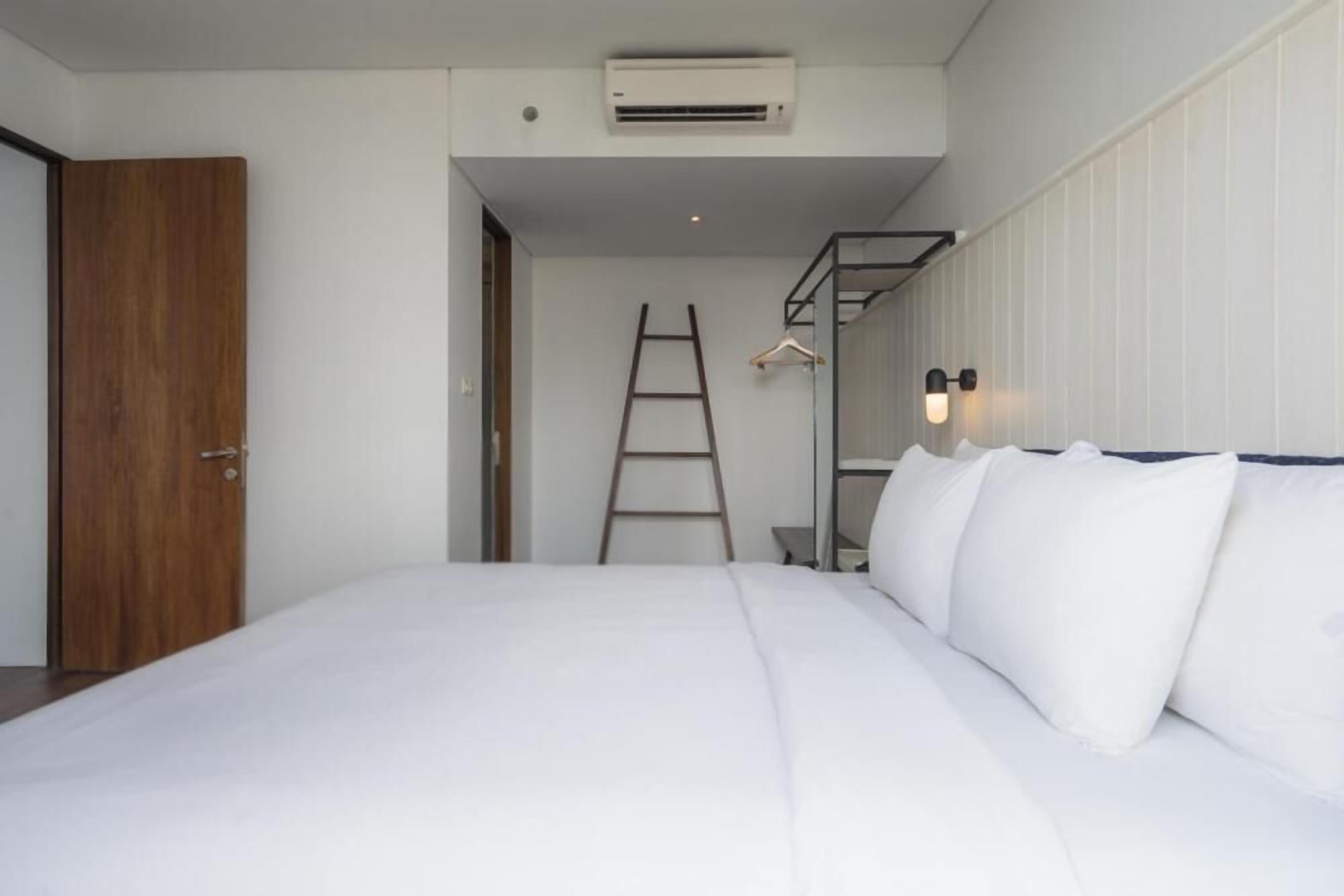 Une chambre à coucher comprenant un lit, une porte en bois, un appareil de climatisation, une échelle et un luminaire fixé au mur.