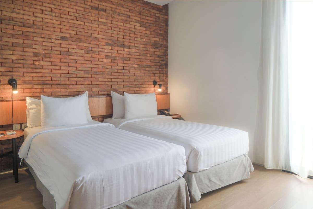 A hotel room with two beds, a brick wall, and a window with curtains.