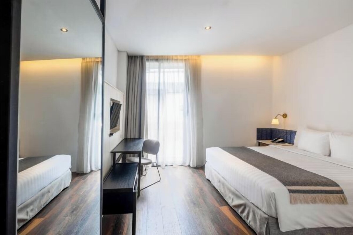 Habitación de hotel con dos camas, un escritorio, una silla, un televisor y una mesita de noche con lámpara.