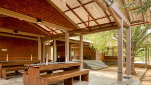 A covered outdoor seating area with wooden benches and tables, stone steps, and a brick wall. - Hide Yala (Thissamaharama)