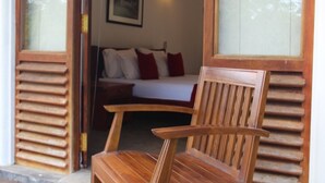 A wooden chair in a room with a bed, a framed picture on the wall, and a window with blinds. - Hide Yala (Thissamaharama)