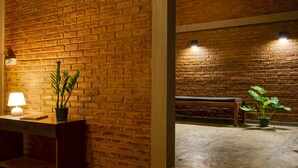 A brick-walled room with a bench, a table with a lamp, and a potted plant. - Hide Yala (Thissamaharama)