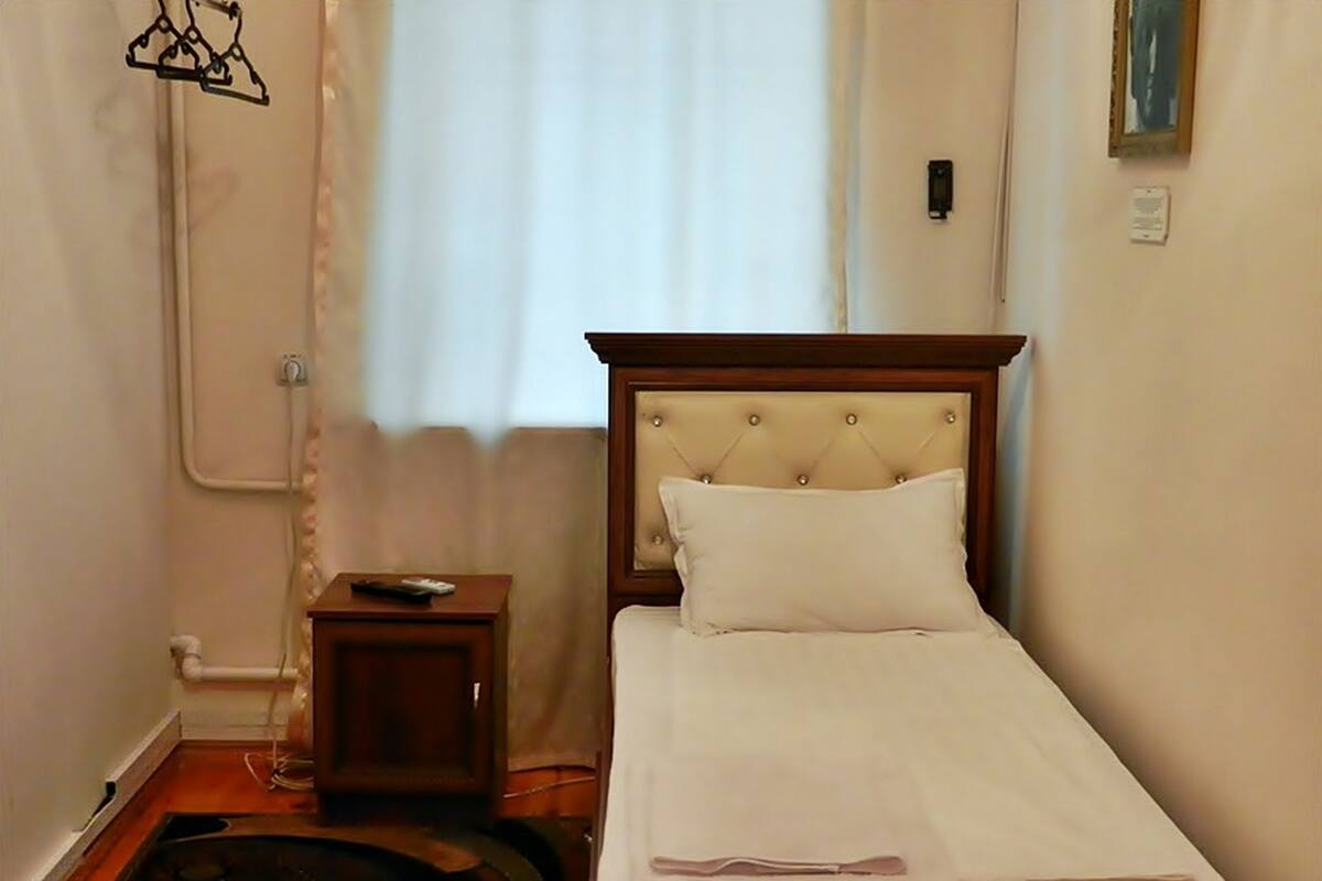A small, neatly arranged bedroom with a single bed, a bedside table, and a window with curtains.