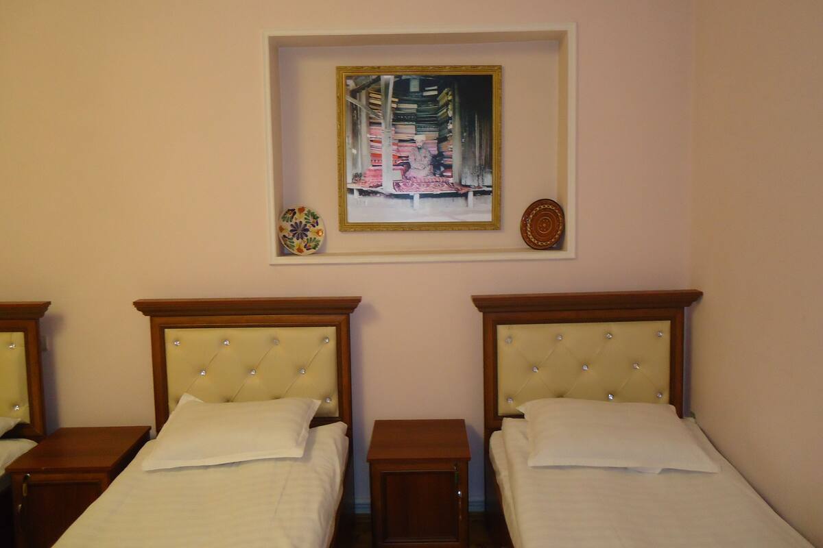 A hotel room with two single beds, a small bedside table, a nightstand, a framed painting, and a decorative plate on the wall.