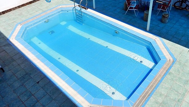 A rectangular swimming pool with a ladder, surrounded by a tiled deck.