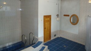 A bathroom with a shower, a wooden door, a mirror, and a light fixture.