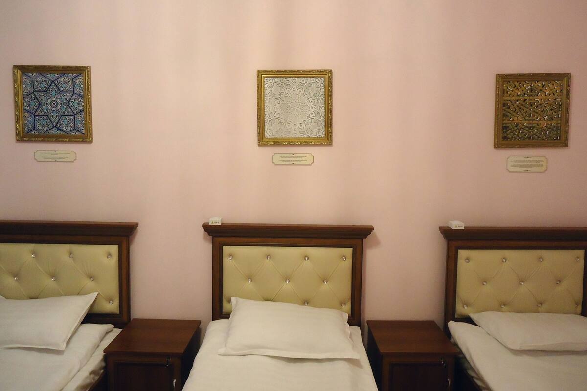 A hotel room with three beds, each with a tufted headboard and white linens. There are decorative wall hangings above each bed.