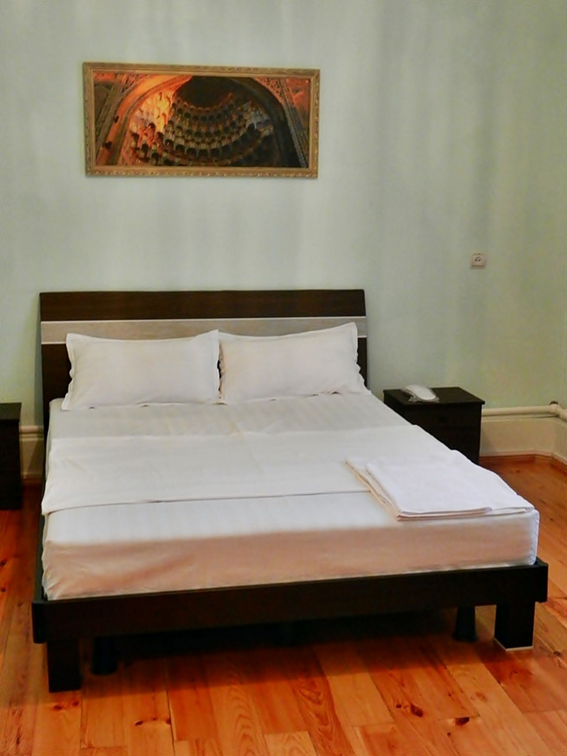 A neatly made bed with white linens, a wooden headboard, and a nightstand with a lamp.