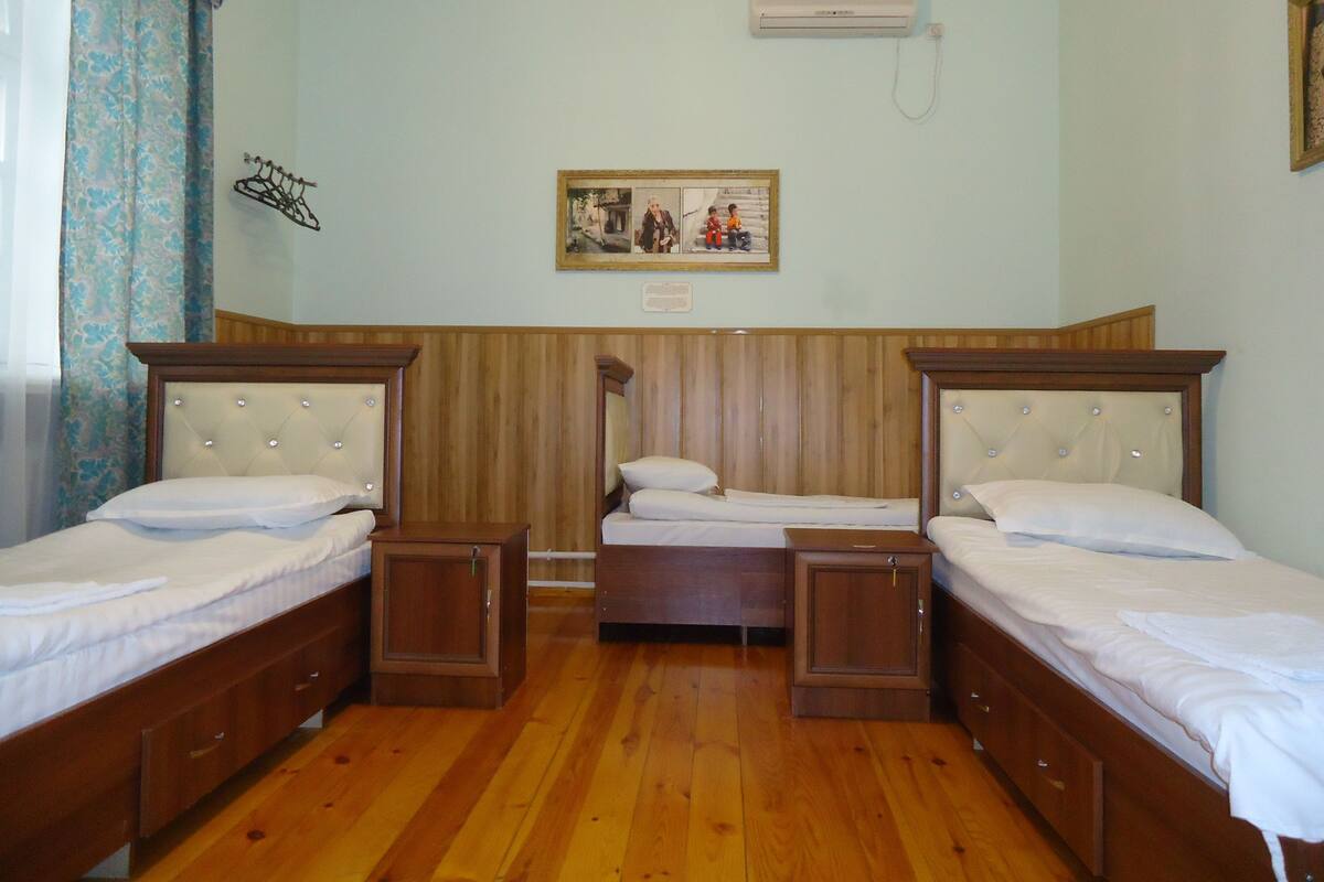 A room with three wooden beds, a wooden wardrobe, a wall-mounted air conditioner, and a framed picture on the wall.