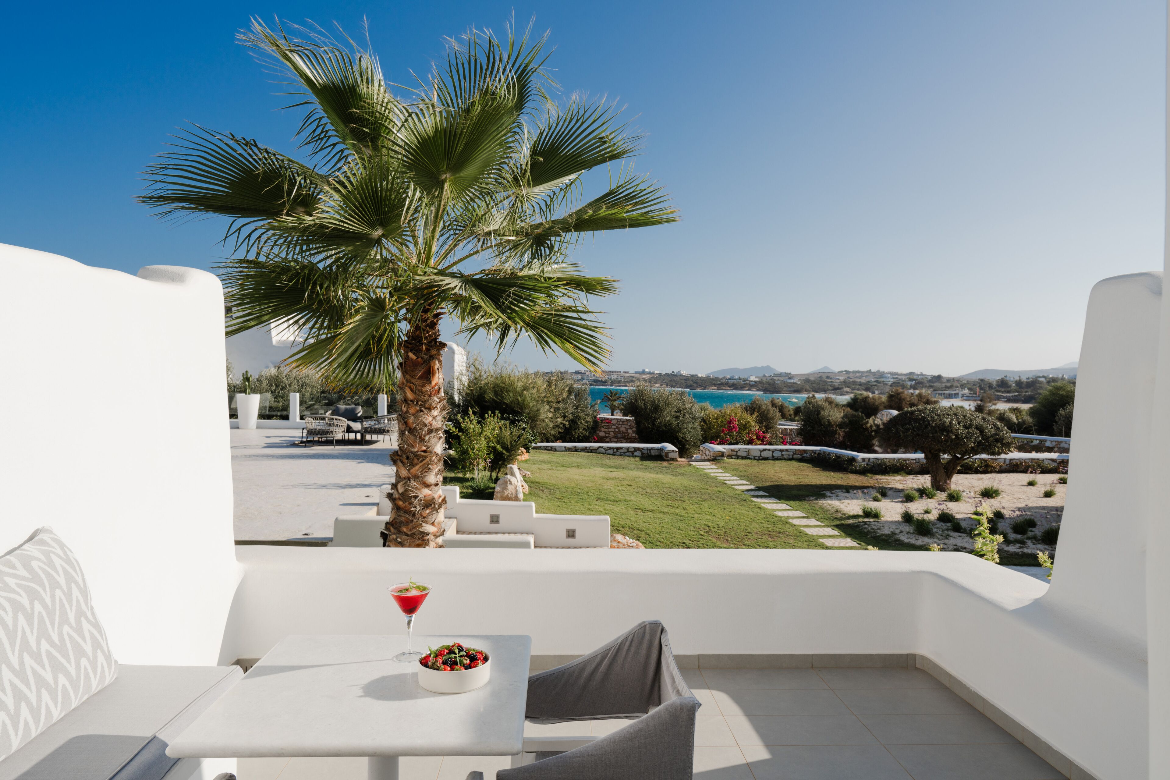 Un balcón con una mesa blanca, una silla, una pequeña planta y vistas al paisaje costero.