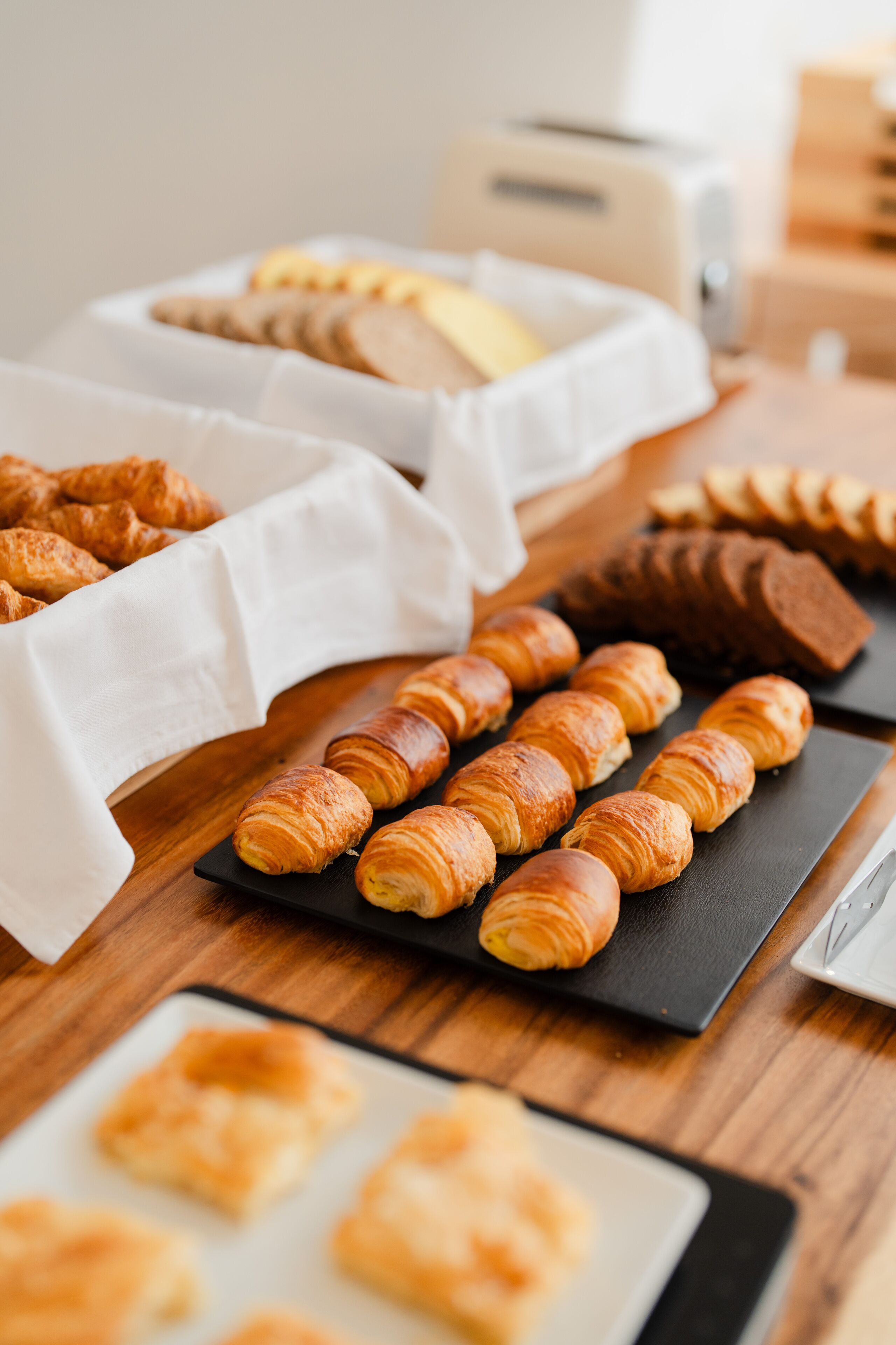 A variety of pastries on a wooden table, including croissants and other baked goods.