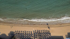 Vista aérea de una playa con hileras de sombrillas y sillas de playa, una orilla arenosa y olas acercándose a la costa.