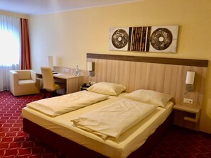 A hotel room with a bed, two bedside tables, a desk with a chair, a lamp, and a window with curtains. - Montana Hotel Köln-Bonn Airport (Troisdorf)