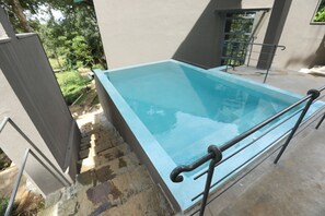 A rectangular swimming pool with a light blue interior, surrounded by a concrete deck and metal railings.