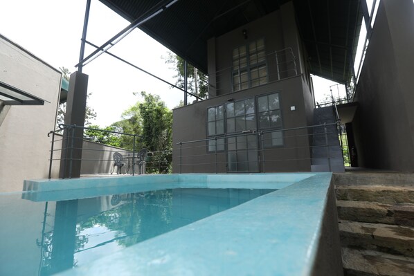 An indoor swimming pool with a clear view of the surrounding architecture, including a modern building with large windows and a covered area with stairs.