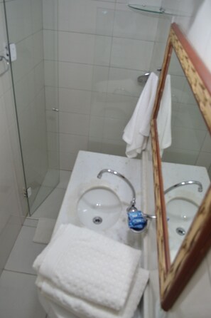 A bathroom with a glass shower enclosure, a white sink with a mirror, and a towel rack.