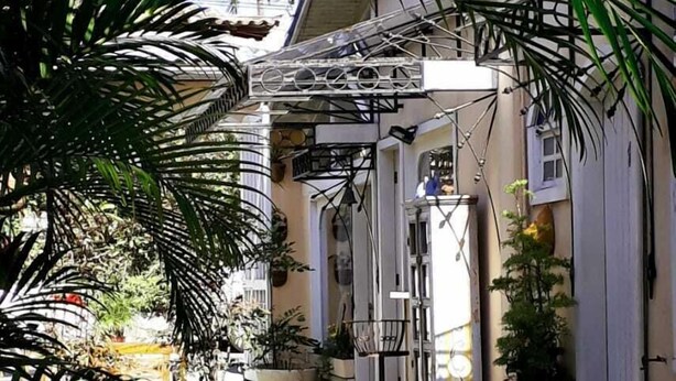 A narrow alleyway with potted plants and a wooden bench. - Pousada Amendoeira (Búzios)