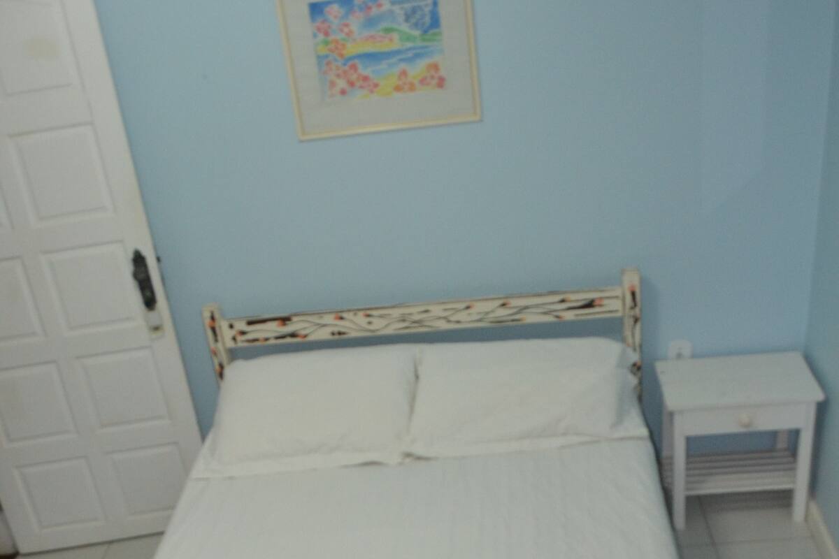 Une chambre à coucher avec un lit, une table de chevet, une porte et un mur orné d’un tableau encadré.