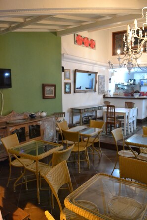 A dining area with wicker chairs and a glass table, a kitchen area with a counter and appliances, and a green wall with framed pictures.